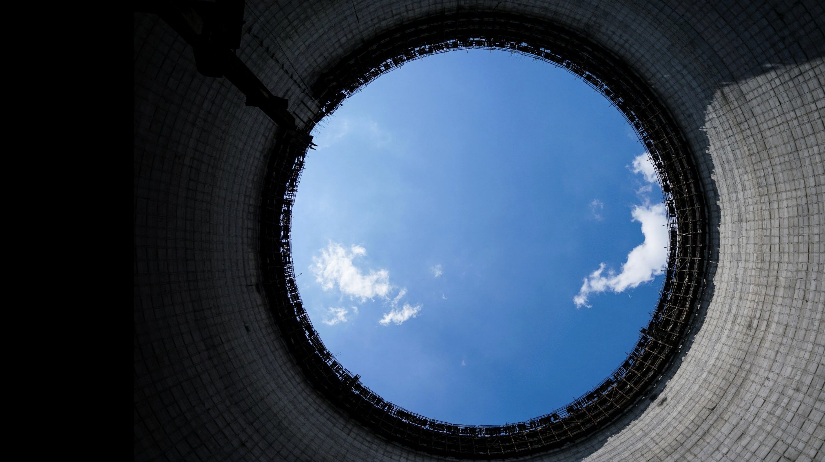 Looking straight up through the open top of a cooling tower under construction to a clear blue sky