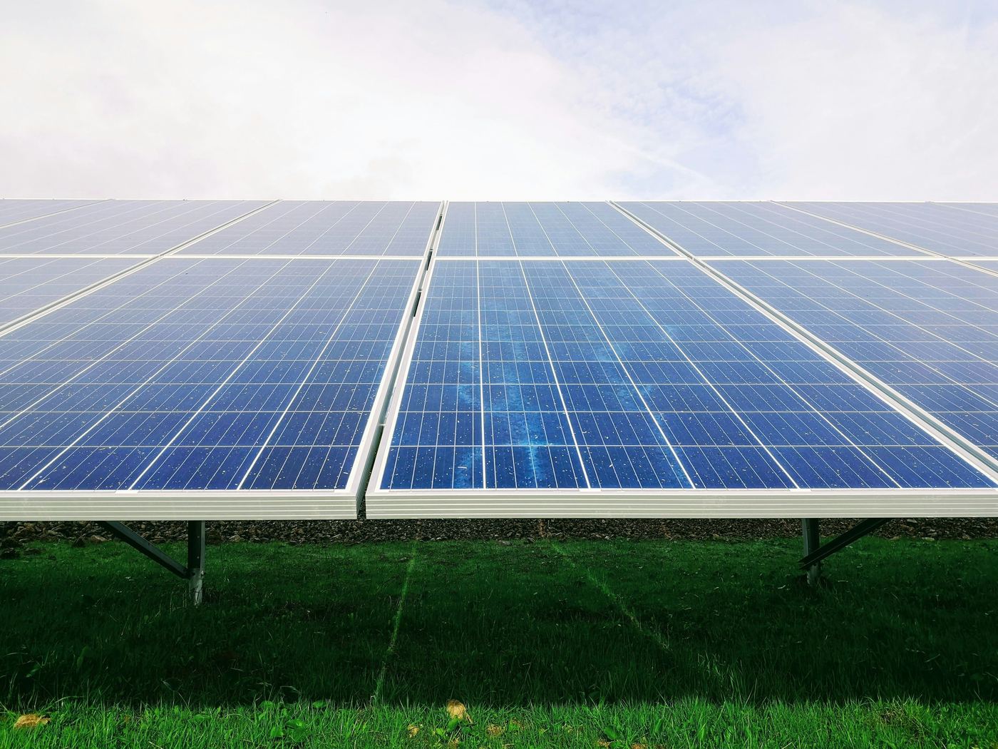 Rows of solar panels on a grass field under an overcast sky